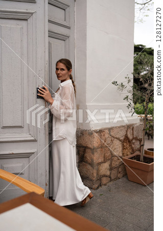 Fashion Model Door: Woman, wearing white, unlocks a grey door outside to enter building during daylight. Fashion Model Door: Woman, wearing white, unlocks a grey door outside to enter building during daylight. 128127270