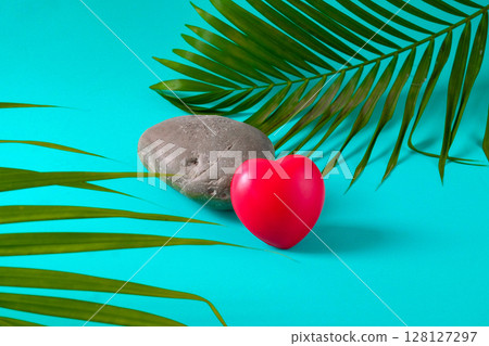 Red heart ball on rock with palm leaves. 128127297