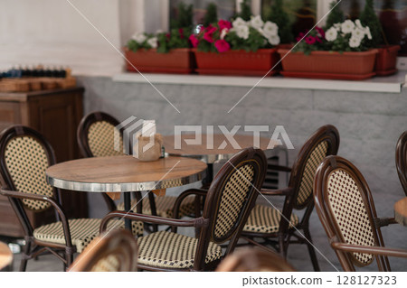 Tables Chairs Flowers: Outdoor cafe seating with wooden chairs, tables, and flowers for relaxed dining anytime. 128127323