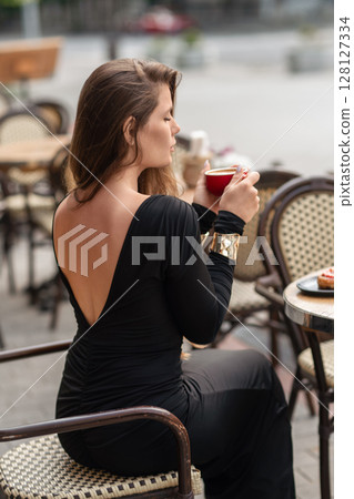 Woman Coffee Dress: Lady drinks coffee at outdoor cafe, daytime, relaxing with drink and cake. 128127334