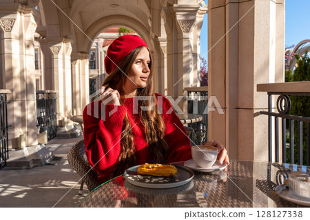 Woman Beret Coffee: Girl enjoys cafe latte and pastry on sunny terrace with arcade backdrop. 128127338