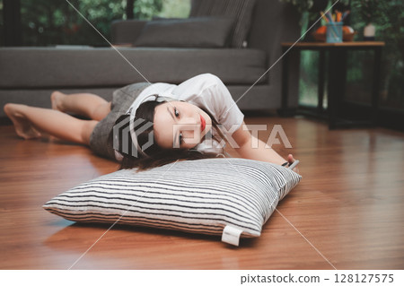 Top view of young beautiful asian woman with headphone and listening music from smartphone while lying on the floor at home. 128127575