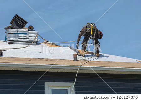 Construction Worker Installing Asphalt Shingles on House Roof Construction Worker Installing Asphalt Shingles on House Roof 128127870