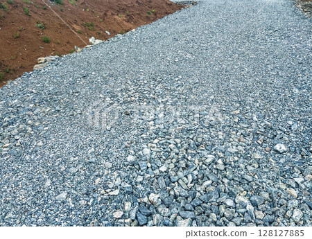 Gravel road surface with small stones and pebbles, leading through a natural landscape, showcasing the texture and composition of the gravel pathway in an outdoor setting 128127885