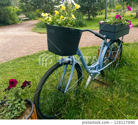 Vintage bicycle with flower planters in baskets, parked on grass, surrounded by greenery, showcasing a blend of nature and urban charm in a serene outdoor setting 128127890