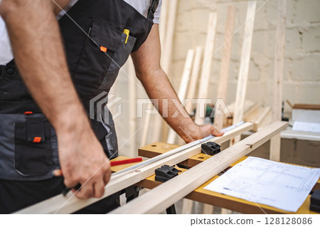 Unrecognizable men measuring wooden plank outdoors 128128086