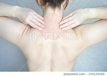 Female adult applying therapeutic patch on upper back for pain relief 128128389