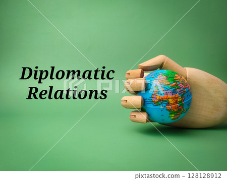 Wooden hand grip the globe with the word Diplomatic Relations on a green background. Wooden hand grip the globe with the word Diplomatic Relations on a green background. 128128912
