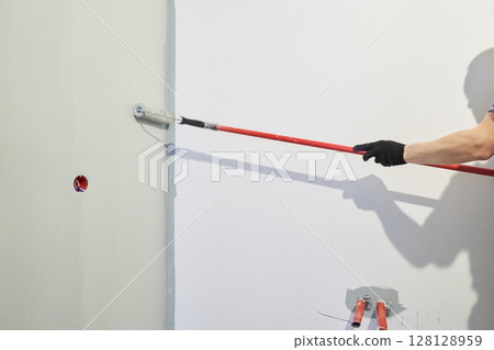 A man paints walls with a roller, working painting on the surface, painting walls in an apartment, repairing with white paint. With space to copy. High quality photo 128128959