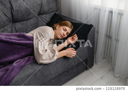 Young woman sleeping peacefully on gray sofa at home. 128128970