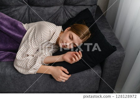 Young woman sleeping peacefully on gray sofa at home. 128128972