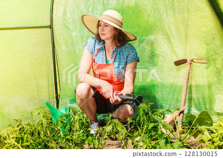 woman with gardening tool working in greenhouse 128130015