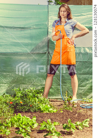 Woman watering the garden with hose 128130074
