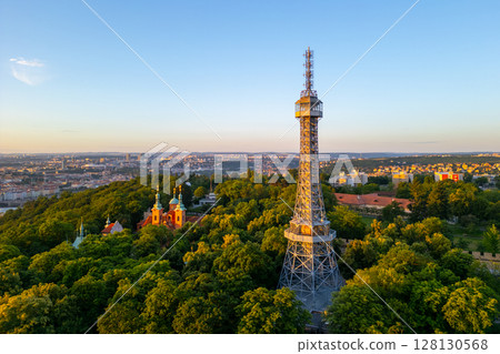 Sunrise casts a warm glow on Petrin Lookout Tower, surrounded by lush greenery and offering a picturesque view of Prague's skyline from the hilltop. 128130568