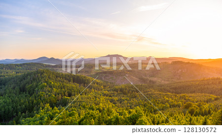 A breathtaking sunset casts golden hues over the Lusatian Mountains, viewed from the heights of Popov Cliffs. Dense forests stretch across the landscape, creating a serene evening atmosphere. A breathtaking sunset casts golden hues over the Lusatian Mountains, viewed from the heights of Popov Cliffs. Dense forests stretch across the landscape, creating a serene evening atmosphere. 128130572