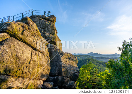 Stunning sandstone rock formations rise at Popov Cliffs in Czechia, bathed in warm evening light, while lush forests stretch into the distance under a clear sky. Stunning sandstone rock formations rise at Popov Cliffs in Czechia, bathed in warm evening light, while lush forests stretch into the distance under a clear sky. 128130574