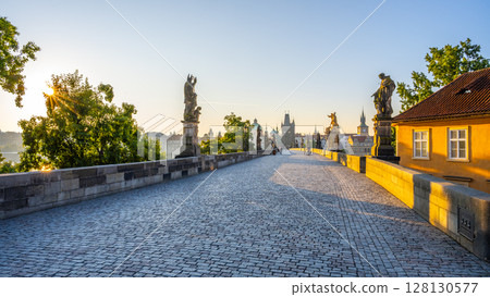 Sunlight illuminates Charles Bridge in Prague as the day begins, casting soft shadows on the cobblestones. The statues stand still, overlooking the peaceful Vltava River and vibrant embankment. Sunlight illuminates Charles Bridge in Prague as the day begins, casting soft shadows on the cobblestones. The statues stand still, overlooking the peaceful Vltava River and vibrant embankment. 128130577