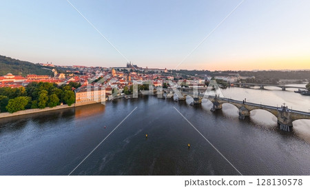 Bright colors fill the sky as the sun rises over Prague, illuminating the Vltava River and its medieval architecture. 128130578