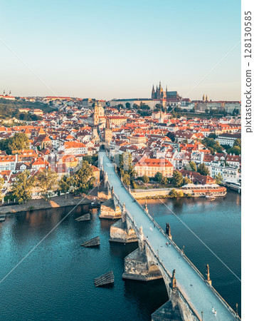 A breathtaking sunrise illuminates the skyline of Prague, showcasing the historic Charles Bridge and the grandeur of Hradcany Castle reflecting on the Vltava River. A breathtaking sunrise illuminates the skyline of Prague, showcasing the historic Charles Bridge and the grandeur of Hradcany Castle reflecting on the Vltava River. 128130585