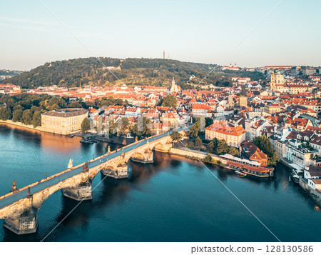 Aerial view captures Charles Bridge bathed in golden light at sunrise. Prague's historic architecture and the Vltava River grace the landscape, creating a serene morning ambiance. Aerial view captures Charles Bridge bathed in golden light at sunrise. Prague's historic architecture and the Vltava River grace the landscape, creating a serene morning ambiance. 128130586