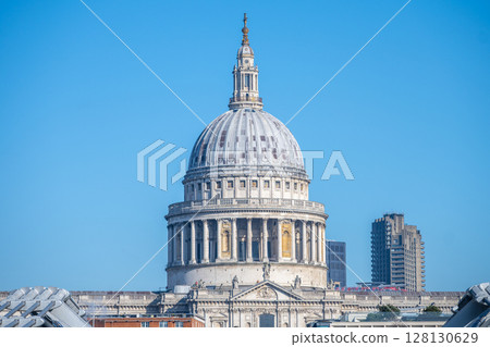 St. Paul's Cathedral's iconic dome stands majestically against a clear blue sky in London. The historic structure showcases intricate architecture and is a significant landmark. 128130629
