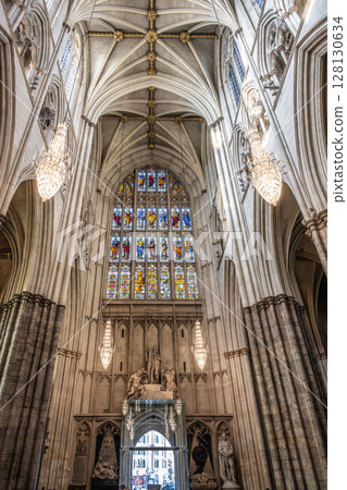 Intricate gothic architecture defines Westminster Abbey, showcasing stunning stained glass windows and elegant chandeliers illuminating the vast interior. Visitors admire the historic beauty. 128130634