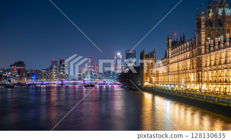 Bright lights illuminate the Palace of Westminster alongside the Thames River. Vauxhall's modern skyscrapers create a striking backdrop against the night sky, showcasing London's stunning skyline. Bright lights illuminate the Palace of Westminster alongside the Thames River. Vauxhall's modern skyscrapers create a striking backdrop against the night sky, showcasing London's stunning skyline. 128130635