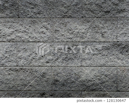 Textured gray stone wall background with a rough surface. The wall features horizontal blocks with varying shades of Textured gray stone wall background with a rough surface. The wall features horizontal blocks with varying shades of 128130647