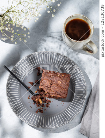 Chocolate brownie with nuts on a dark plate on a light background with cup of coffee 128130739
