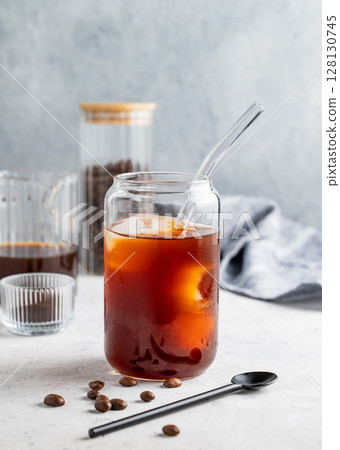 Cold brew coffee in a glass with ice on a light background with coffee beans and spoon. 128130745