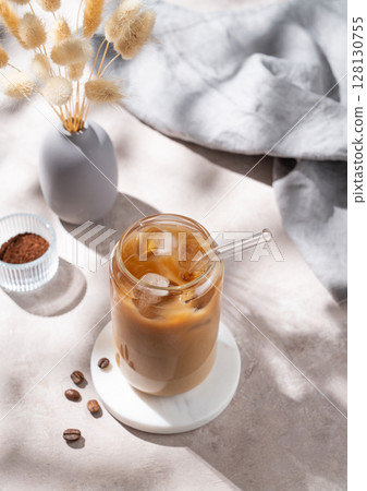 Ice latte coffee in a glass with milk on a light background with coffee beans, dry bouquet flowers Ice latte coffee in a glass with milk on a light background with coffee beans, dry bouquet flowers 128130755