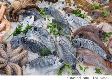 Bustling fish market in Greece displays abundant seafood like fresh fish, octopus, and various shellfish on ice, emphasizing local culinary traditions. 128130869