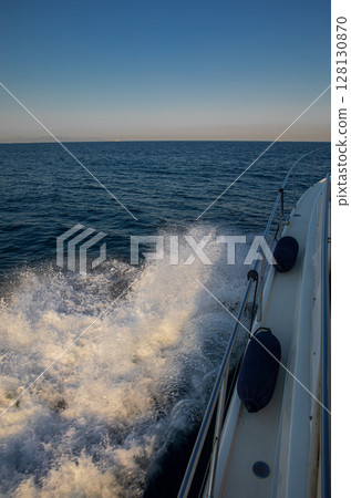 Sailboat navigating through calm waters of Greece, creating waves and splashes, showcasing beautiful blue seascape under clear sky, ideal for travel adventures. Sailboat navigating through calm waters of Greece, creating waves and splashes, showcasing beautiful blue seascape under clear sky, ideal for travel adventures. 128130870