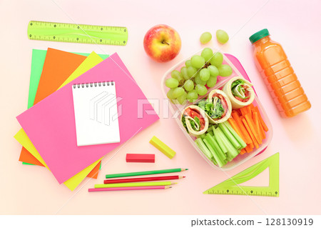 Healthy lunch features colorful wraps filled with vegetables, grapes, apple, and drink alongside bright stationery. Perfect setting for school or study time preparation. Healthy lunch features colorful wraps filled with vegetables, grapes, apple, and drink alongside bright stationery. Perfect setting for school or study time preparation. 128130919