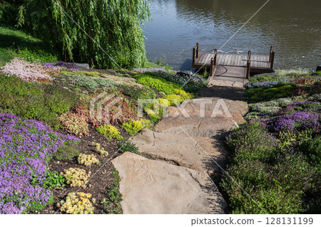 A stunning Scenic Riverbank Garden adorned with Vibrant Flowers and a charming Wooden Dock A stunning Scenic Riverbank Garden adorned with Vibrant Flowers and a charming Wooden Dock 128131199