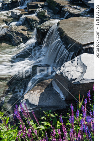 A Beautiful Tranquil Waterfall Flowing Gracefully Over Rocks Surrounded by Vibrant Flowers A Beautiful Tranquil Waterfall Flowing Gracefully Over Rocks Surrounded by Vibrant Flowers 128131355