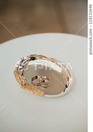 Pair of classic yellow gold wedding bands resting on ornate silver tray Pair of classic yellow gold wedding bands resting on ornate silver tray 128131646