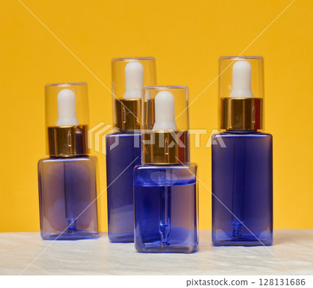 Transparent square blue bottles with gold caps and white pipettes 128131686