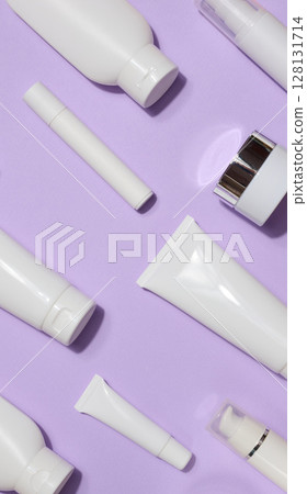 A variety of white plastic tubes and bottles with cosmetics arranged randomly on a lavender background. Top view 128131714