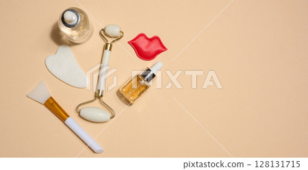 Set of cosmetics and skin care tools including facial massagers, decorative lips and serum bottles placed on beige background. Set of cosmetics and skin care tools including facial massagers, decorative lips and serum bottles placed on beige background. 128131715