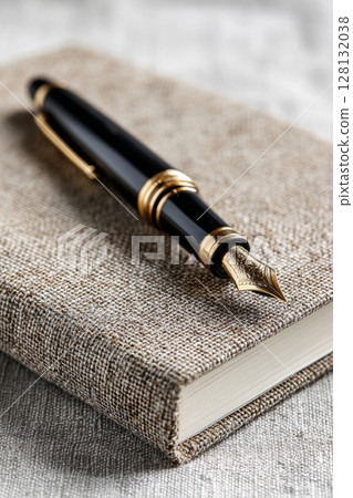 Fountain pen with gold accents on textured fabric covered notebook 128132038