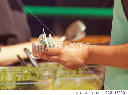 Person Holding Cash Against Culinary Background at Food Market 128132630