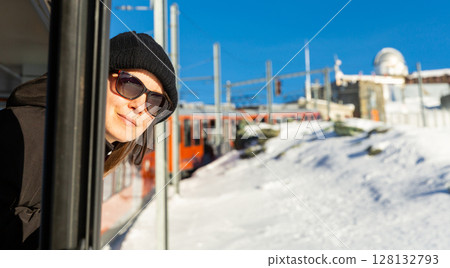 Happy woman in sunglasses sticking head out of train window passing among snowy areas 128132793