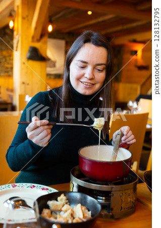 Woman eating fondue with piece of bread and special fork 128132795