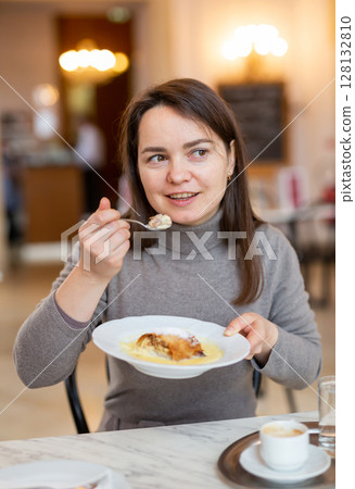 Cheerful woman enjoying apple strudel with espresso in coffee house 128132810