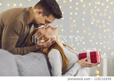 Loving man standing behind and kissing his girlfriend on the forehead, who is sitting on the couch. Loving man standing behind and kissing his girlfriend on the forehead, who is sitting on the couch. 128132836