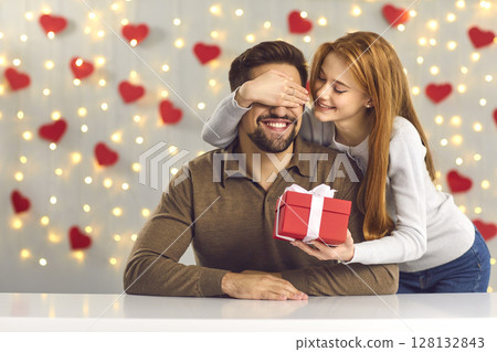 Happy young man getting present from his loving girlfriend on Saint Valentine's Day Happy young man getting present from his loving girlfriend on Saint Valentine's Day 128132843