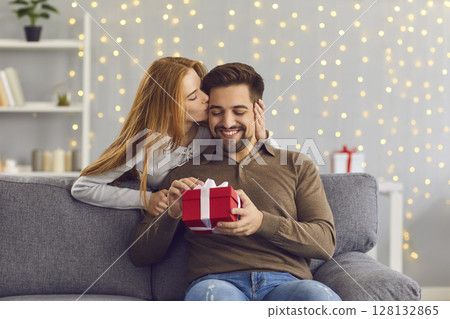 Woman from behind hugs and kisses her beloved husband giving him a gift on this special day. Woman from behind hugs and kisses her beloved husband giving him a gift on this special day. 128132865