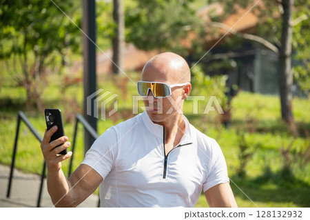 Caucasian cyclist taking selfie on smart phone in park. Outdoor activity. 128132932
