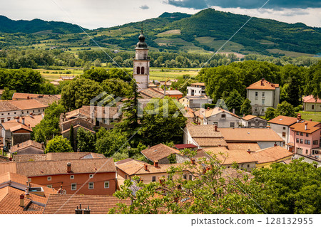 Picturesque View Of Vipava From Castle Ruins: Red-Tiled Rooftops And Church Tower Nestled In Green Valley With Blooming Flowers In Foreground And Rolling Fields In Background, Slovenia 128132955